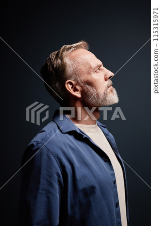 Vertical side view portrait of bearded senior man wearing casual clothes looking up in studio 115315971