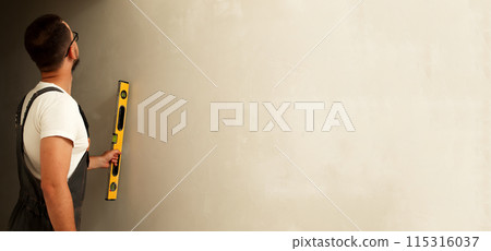 Man using level tool on wall, ample copy space, ideal for banner design and templates. Construction worker with level tool, white wall, blank area for text 115316037