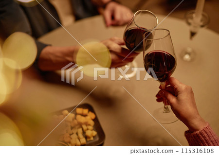 High angle closeup of adult couple toasting with wine glasses over table enjoying romantic dinner date with bokeh effect copy space 115316108