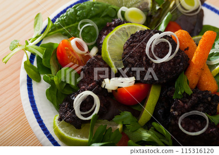 Blood sausage with different greens, tomatoes and lemon served at plate Blood sausage with different greens, tomatoes and lemon served at plate 115316120