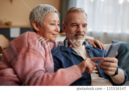 Portrait of smiling senior couple using phone together and tapping screen with mobile app at home Portrait of smiling senior couple using phone together and tapping screen with mobile app at home 115316147