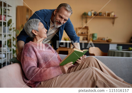 Portrait of happy senior couple at home together with woman reading book relaxing on sofa copy space Portrait of happy senior couple at home together with woman reading book relaxing on sofa copy space 115316157