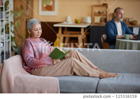 Full length portrait of senior woman reading book relaxing on couch at home and enjoying retirement copy space 115316159