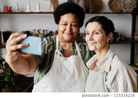 Warm toned portrait of two smiling mature women taking selfie photo with smartphone in pottery studio, copy space Warm toned portrait of two smiling mature women taking selfie photo with smartphone in pottery studio, copy space 115316228