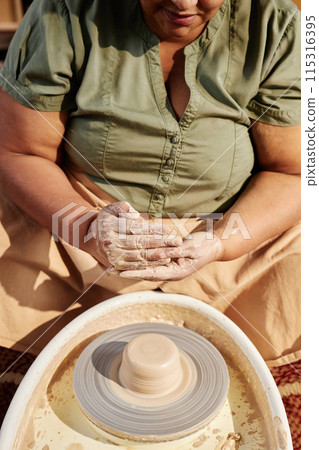 Vertical closeup of senior African American woman enjoying pottery class in sunlight and shaping clay 115316395