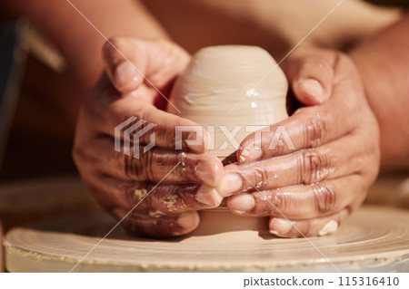 Front view closeup of gentle female hands shaping clay on pottery wheel enjoying crafting process in sunlight Front view closeup of gentle female hands shaping clay on pottery wheel enjoying crafting process in sunlight 115316410