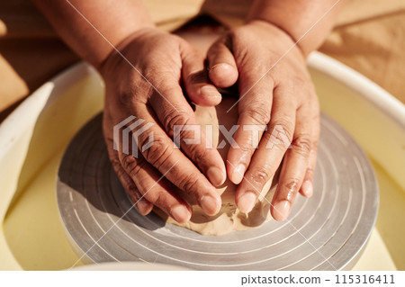 Close up of female hands carefully shaping clay on pottery wheel and making ceramics in sunlight copy space Close up of female hands carefully shaping clay on pottery wheel and making ceramics in sunlight copy space 115316411