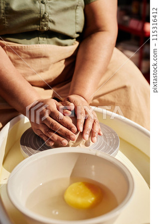 Vertical closeup of unrecognizable Black woman carefully shaping clay on pottery wheel enjoying ceramics class in sunlight Vertical closeup of unrecognizable Black woman carefully shaping clay on pottery wheel enjoying ceramics class in sunlight 115316412