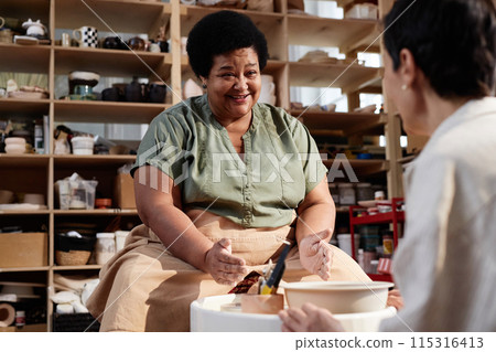 Portrait of smiling senior African American woman enjoying pottery class in cozy studio lit by sunlight copy space 115316413