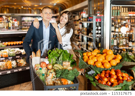 Portrait of a happy young couple with products in a cart in the supermarket 115317675