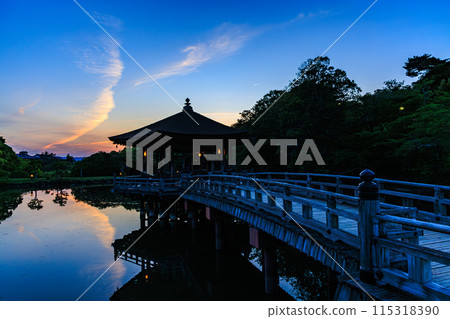 Evening view of Ukimido at Sagiike Pond in Nara Park. Thin clouds radiating from Mt. Ikoma against the backdrop of the sunset and Ukimido casting its shadow on the water. 115318390