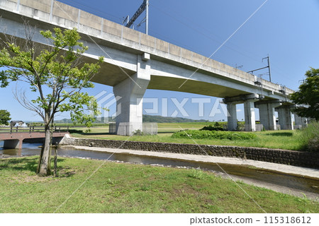 Park scenery with railroad tracks, stream and bridge 115318612