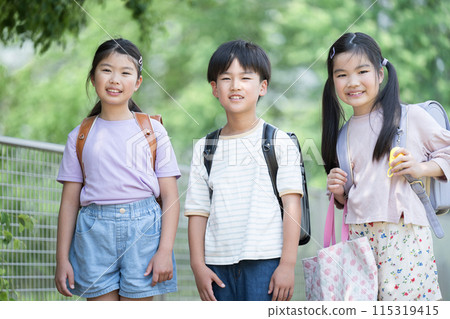 小學生背著書包在美麗的新綠中步行上學，親密的同學看著鏡頭 115319415