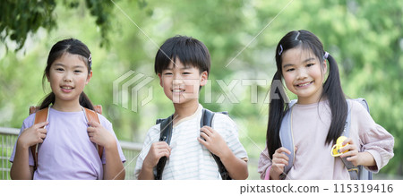 小學生背著書包在美麗的新綠中步行上學，親密的同學看著鏡頭 115319416