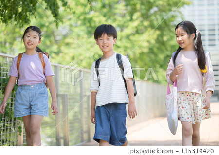 照片中，小學生背著書包在美麗的新鮮綠色植物中步行上學，親密的同學看著鏡頭 115319420