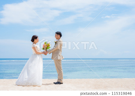 Bride and groom holding a bouquet by the tropical sea Bride and groom holding a bouquet by the tropical sea 115319846