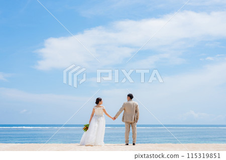 Bride and groom holding a bouquet by the tropical sea 115319851