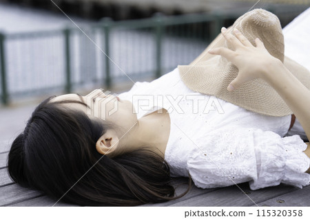 A woman in a white dress lying on a wooden deck by the sea A woman in a white dress lying on a wooden deck by the sea 115320358