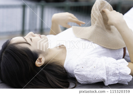A woman in a white dress lying on a wooden deck by the sea 115320359
