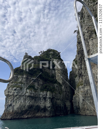 A ladder of a boat in front of huge rock formations on the sea A ladder of a boat in front of huge rock formations on the sea 115320637