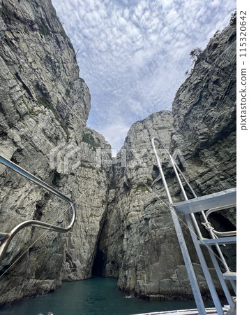 A ladder of a boat in front of huge rock formations on the sea A ladder of a boat in front of huge rock formations on the sea 115320642