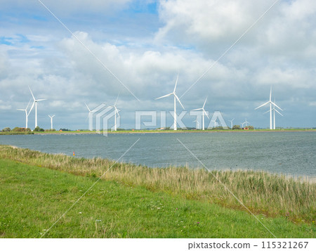 Makkum, Netherlands - August 6th 2024: Wind generators situated directly at the coast. Makkum, Netherlands - August 6th 2024: Wind generators situated directly at the coast. 115321267
