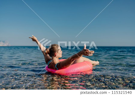 A woman is floating on a pink inflatable raft in the ocean 115321540