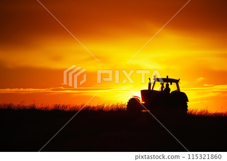 Harvest Harmony: High-Contrast Silhouette of a Farm Tractor at Sunrise 115321860