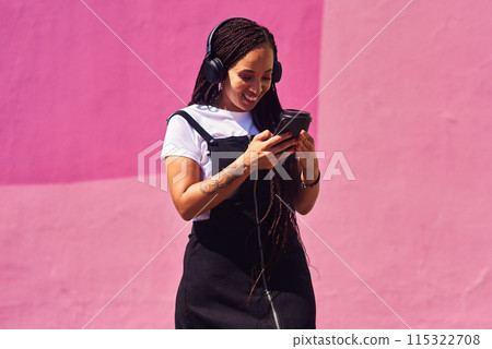 Woman, phone and outdoor for music or tea, streaming sound and subscription by pink background. Female person, coffee and listening to podcast or mockup space, communication and travel to relax 115322708