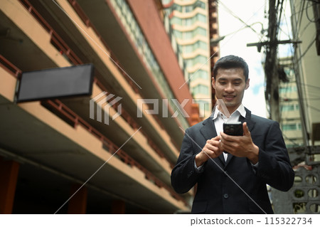 Handsome businessman in formal wear walking on city street and using smartphone Handsome businessman in formal wear walking on city street and using smartphone 115322734