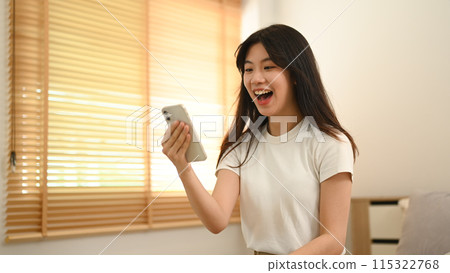 Pretty Asian woman looking at smartphone screen feeling surprise and excitedly Pretty Asian woman looking at smartphone screen feeling surprise and excitedly 115322768