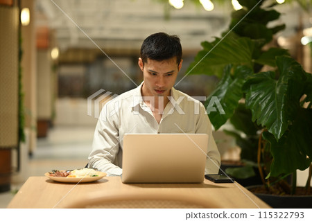 Focused businessman working with laptop during lunch time at cafeteria 115322793