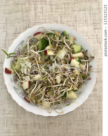 Salad of fresh vegetables and microgreens. Onions, apples, a mound of sprouted mung beans on a porcelain white plate on the table. Concept of diet, veganism, healthy foods. Close-up 115323125