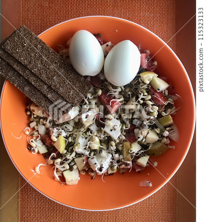 Salad of fresh vegetables and fenugreek sprouts microgreens, eggs, bread, in an orange bowl on the table. Concept of diet, vegan, healthy products. Close-up. 115323133