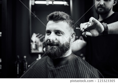 A man with a beard is getting his hair cut by a barber A man with a beard is getting his hair cut by a barber 115323305