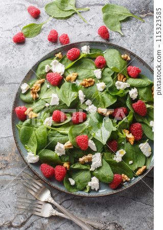 Summer salad of spinach, raspberries, feta and walnuts close-up in a plate. Vertical top view 115323585