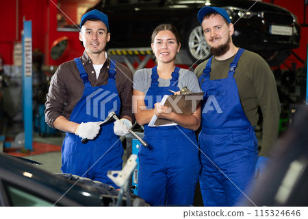 Two guys and woman mechanics posing at car service station Two guys and woman mechanics posing at car service station 115324646