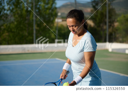 Middle-aged woman playing tennis on an outdoor court on a sunny day 115326550