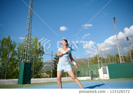 Middle-aged woman playing tennis on a sunny day at an outdoor court Middle-aged woman playing tennis on a sunny day at an outdoor court 115326572