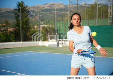 Middle-aged woman playing tennis on an outdoor court 115326595