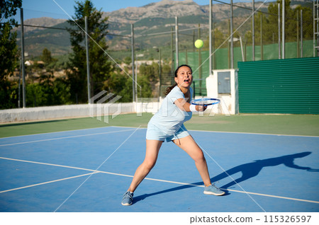 Woman in her 40s playing tennis on an outdoor court with determination 115326597