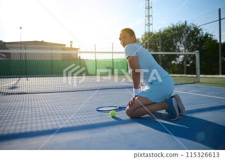 Middle-aged woman playing tennis on outdoor court during sunny day 115326613