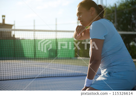 Middle-aged woman playing tennis on court, taking break under sunlight Middle-aged woman playing tennis on court, taking break under sunlight 115326614