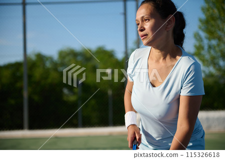 Middle-aged woman playing tennis on an outdoor court in daytime Middle-aged woman playing tennis on an outdoor court in daytime 115326618
