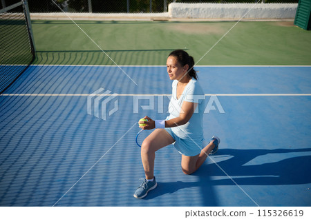 Woman tennis player in her 40s playing tennis on the court, holding tennis ball and racket Woman tennis player in her 40s playing tennis on the court, holding tennis ball and racket 115326619