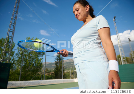Woman in her 40s enjoying a game of tennis on a sunny outdoor court 115326628