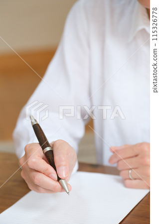 A middle-aged woman writing a letter to her family in the living room 115326778