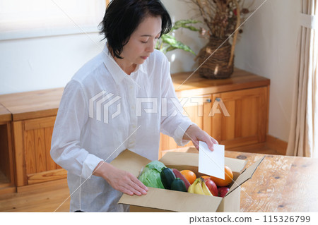 A middle-aged woman putting a letter into a cardboard box for remittance A middle-aged woman putting a letter into a cardboard box for remittance 115326799