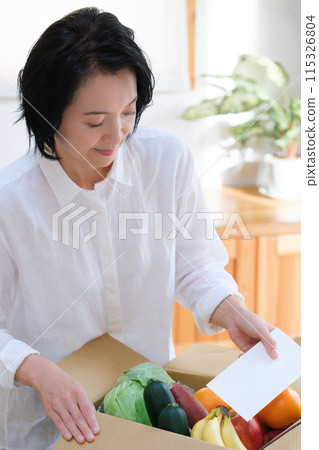 A middle-aged woman putting a letter into a cardboard box for remittance 115326804