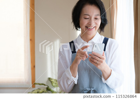 A middle woman who operates a smartphone in the living room A middle woman who operates a smartphone in the living room 115326864